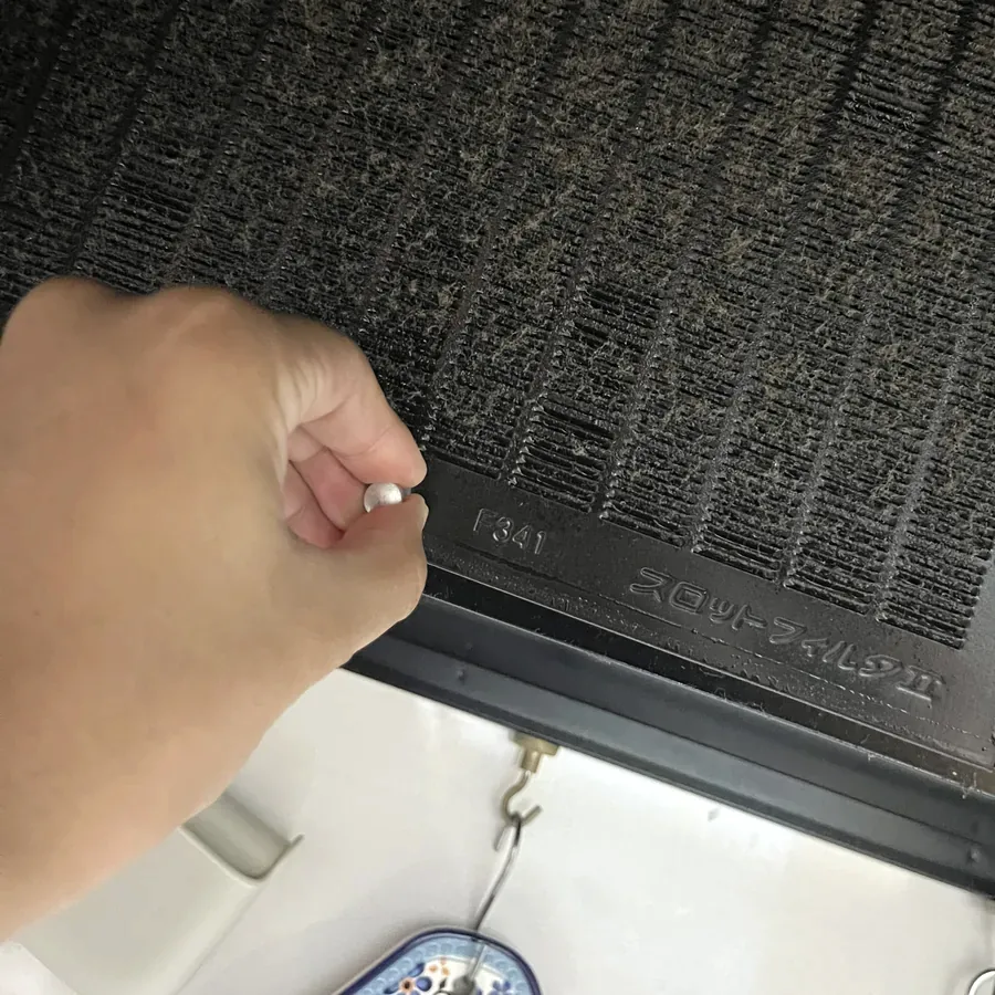 換気扇のフィルターのツマミをつまんで外す手元